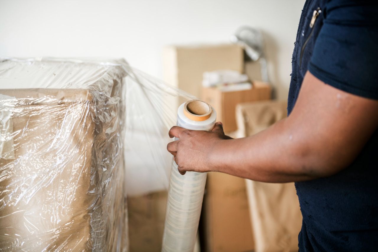 Personne utilisant un film plastique pour envelopper des cartons dans un entrepôt logistique.