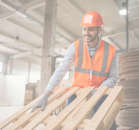 Employé en gilet de sécurité et casque manipulant une palette en bois dans un entrepôt.